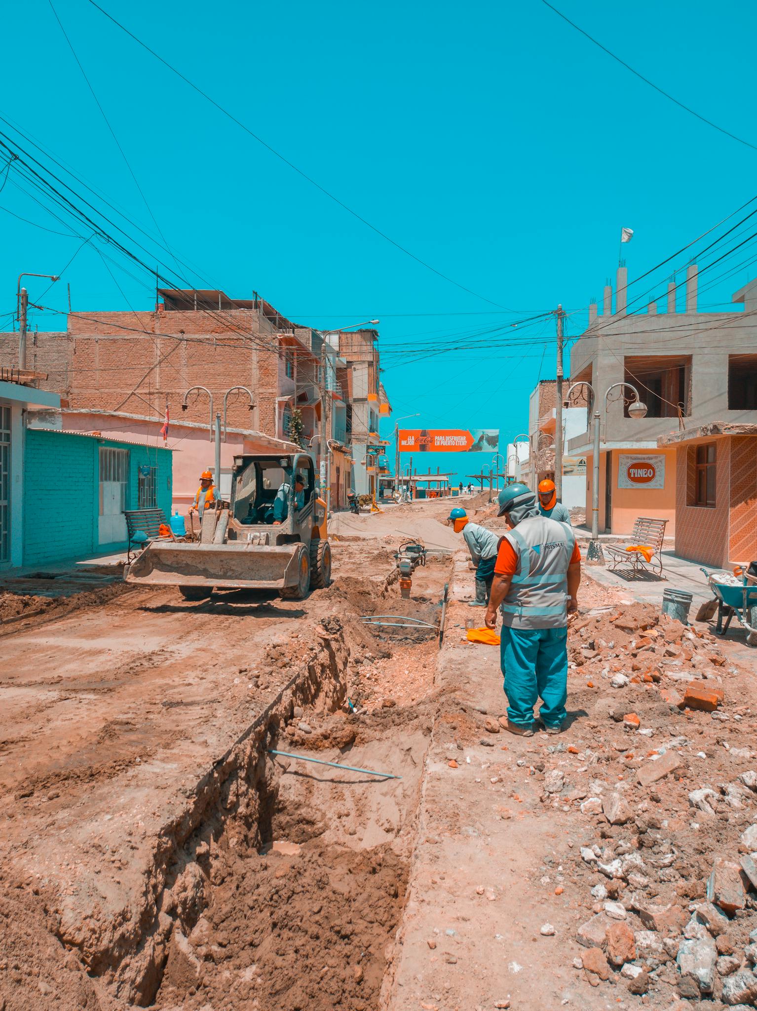 Workers engage in road construction under clear blue skies in a city street.